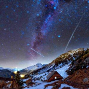 La Voie lactée s’élève dans le ciel nocturne au-dessus d’un paysage de montagne sombre et vallonné, vue depuis le refuge de Cuchet. Une lumière diffuse éclaire la vallée, avec un sentier serpentant au premier plan et la Dent Parrachée en toile de fond.