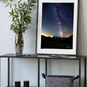 Photographie encadrée du Col de l’Iseran sous un ciel étoilé avec la Voie Lactée et Jupiter visibles, prise de nuit en 2020, avec le panneau emblématique au premier plan.