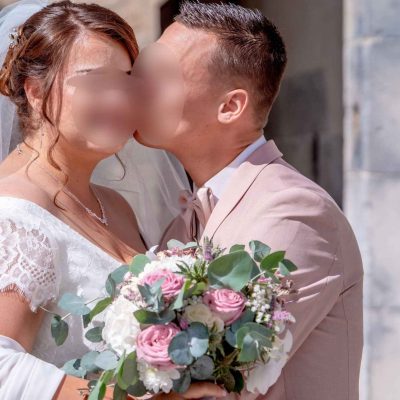 Un marié embrasse tendrement sa femme sur la joue, bouquet à la main, juste après la cérémonie de mariage.