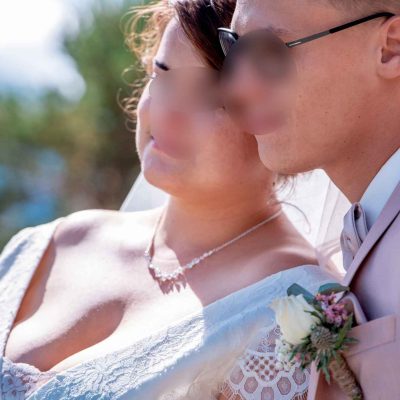 Les mariés, proches l’un de l’autre, regardent ensemble dans la même direction sous un ciel bleu, baignés de lumière naturelle.