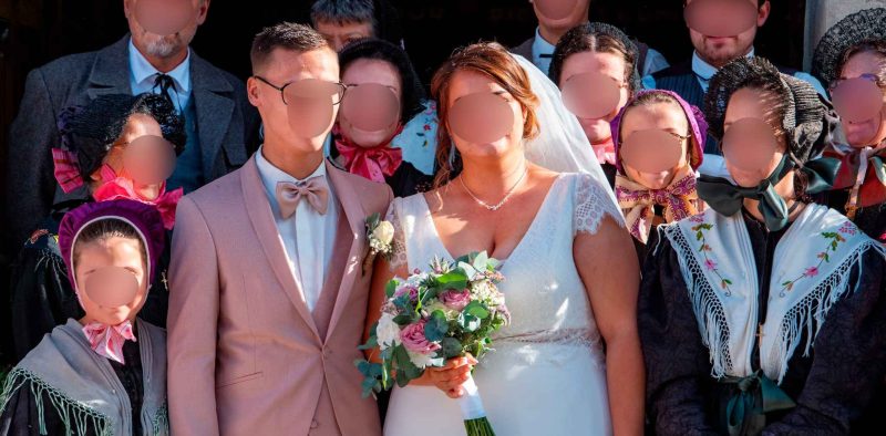 Les mariés posent entourés de leurs invités vêtus de costumes traditionnels savoyards, devant l’église, en pleine lumière.