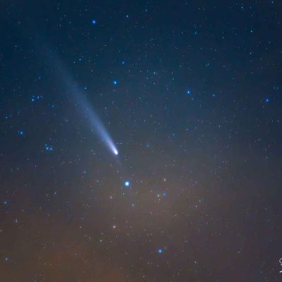 Comète lumineuse avec une longue traînée dans un ciel étoilé, entourée de constellations visibles sur un fond bleu profond.