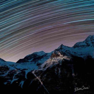 Traînées d’étoiles colorées dans le ciel nocturne au-dessus de sommets enneigés, formant un arc lumineux par empilement de plusieurs poses longues.