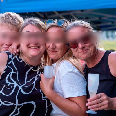 Invitées souriantes posant ensemble sous un barnum lors d’un mariage estival, chacune tenant un verre à la main.