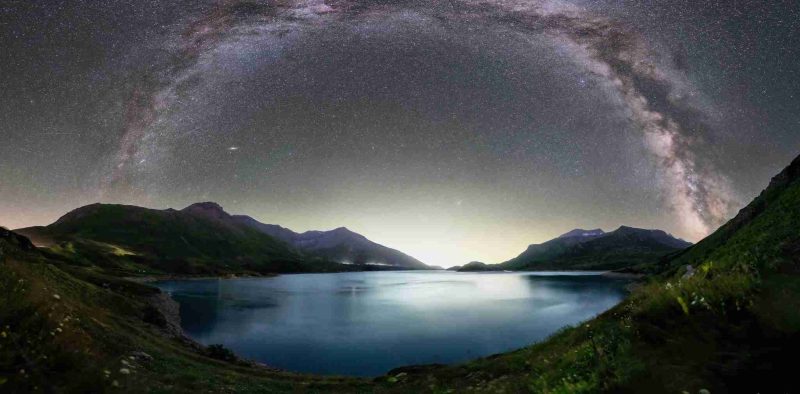 Lac de montagne paisible bordé de collines vertes, surplombé par un arc complet de la Voie lactée sous un ciel étoilé.